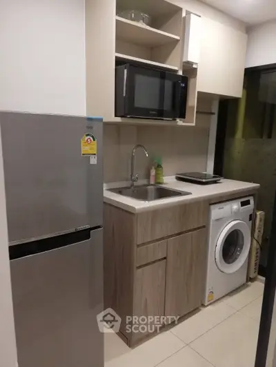 Modern compact kitchen with appliances including fridge, microwave, and washing machine.