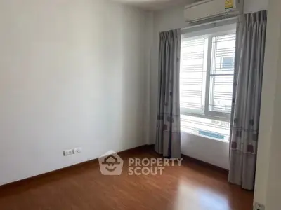 Bright empty room with wooden flooring and large window, perfect for customization.