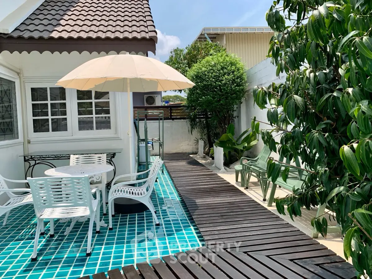 Charming outdoor patio with poolside seating and lush greenery, perfect for relaxation and entertaining.