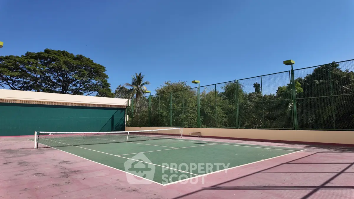Spacious outdoor tennis court with lush greenery and clear blue sky, perfect for sports enthusiasts.