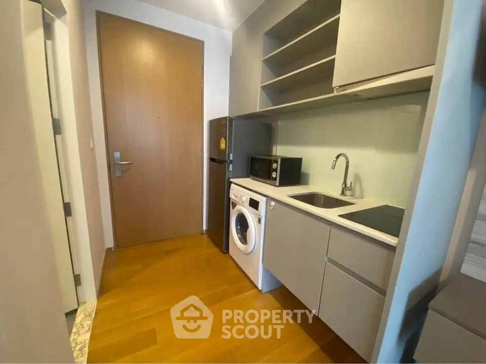 Compact modern kitchen with washing machine and microwave, sleek cabinetry and wooden flooring.