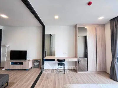 Modern bedroom with sleek wooden furniture and TV, featuring a stylish workspace and large mirror.