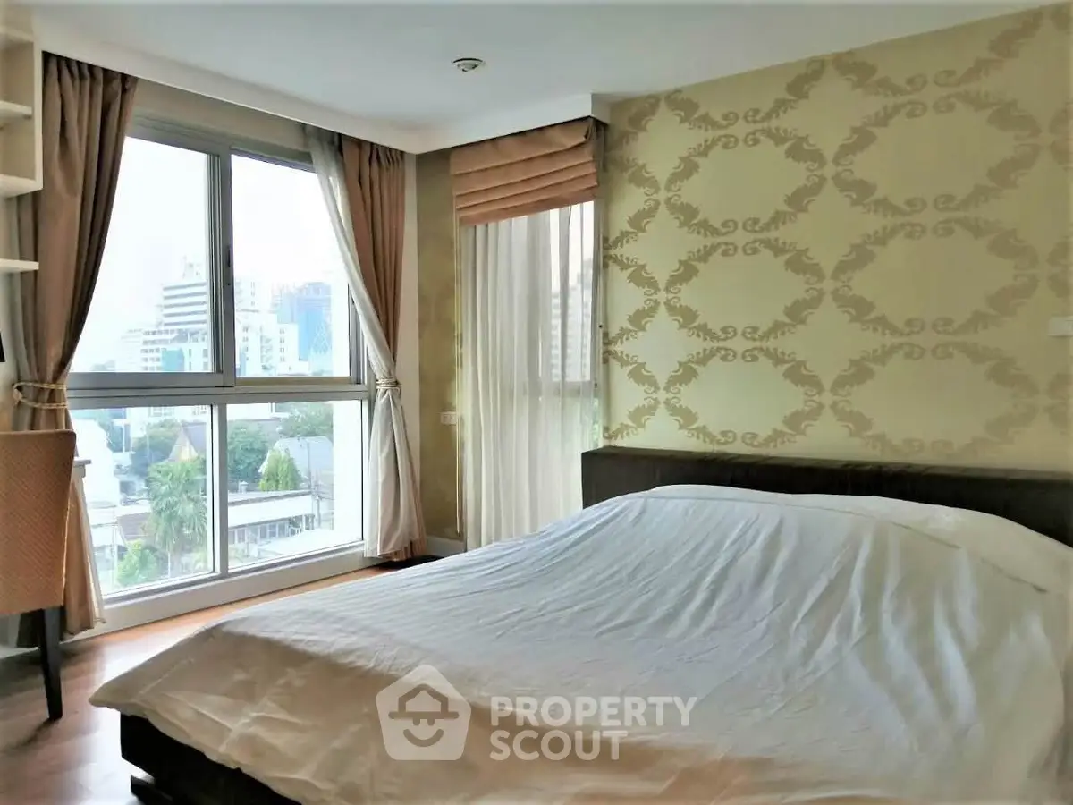 Spacious bedroom with large windows offering city views and elegant wallpaper design.