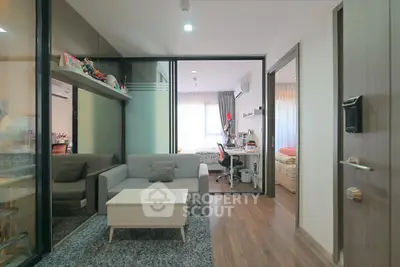 Modern living room with glass partition leading to a cozy bedroom, featuring stylish furniture and wooden flooring.