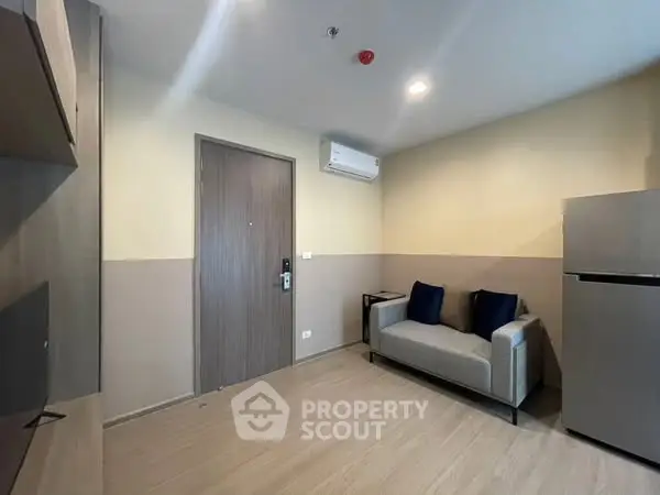 Modern living room with sleek design and neutral tones, featuring a compact sofa and wall-mounted TV.