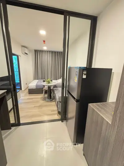 Modern studio apartment with sliding glass doors, featuring a cozy bedroom and compact kitchen area.