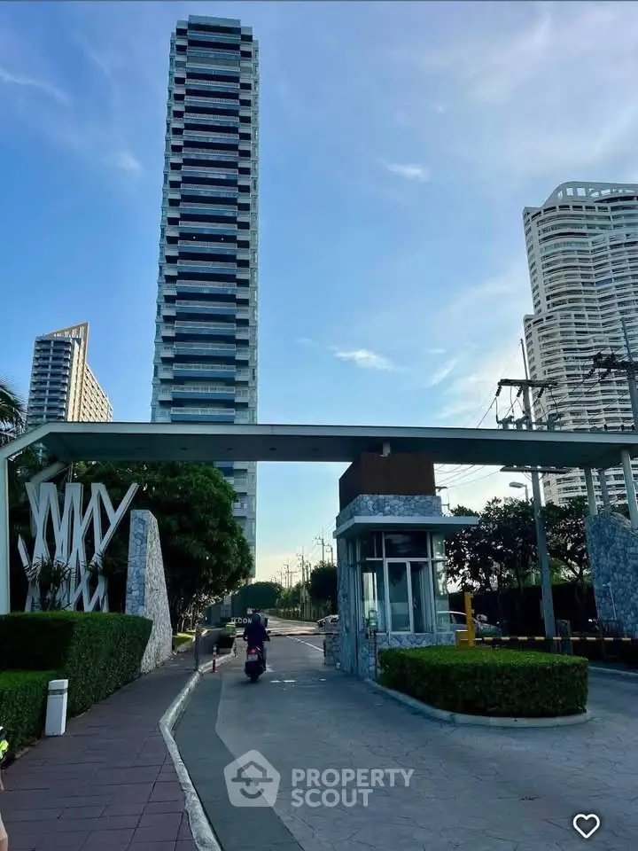 Modern high-rise building entrance with lush greenery and clear sky