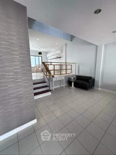 Spacious modern living area with tiled flooring and stylish staircase, perfect for contemporary living.