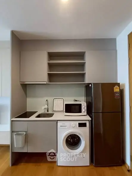 Modern compact kitchen with washing machine, fridge, and microwave in sleek design.