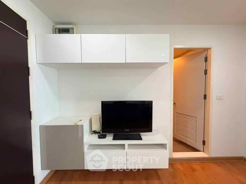 Modern living room with sleek white cabinetry and flat-screen TV on wooden flooring.