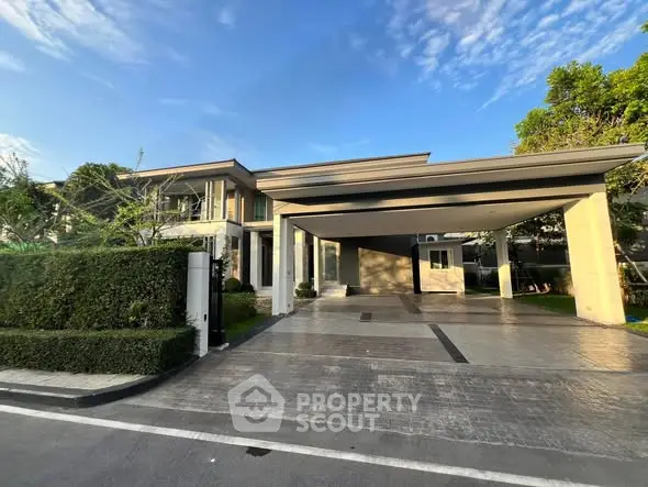 Luxurious modern house with spacious driveway and lush greenery under a clear blue sky.