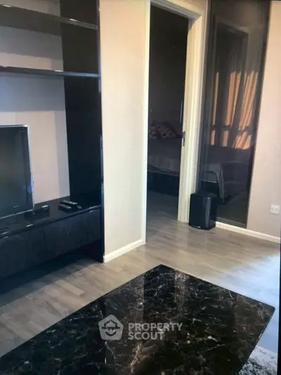 Modern living room with sleek black furniture and a glimpse into a cozy bedroom.