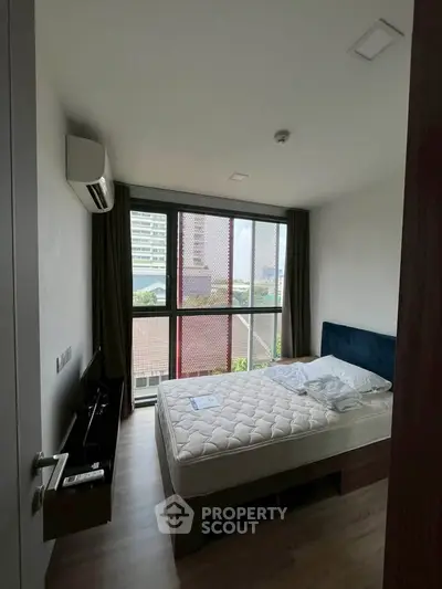 Modern bedroom with large window and city view, featuring a comfortable bed and sleek design.