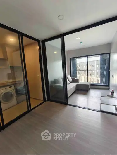 Modern apartment with glass partitions and cozy living area, featuring a washing machine and large windows.