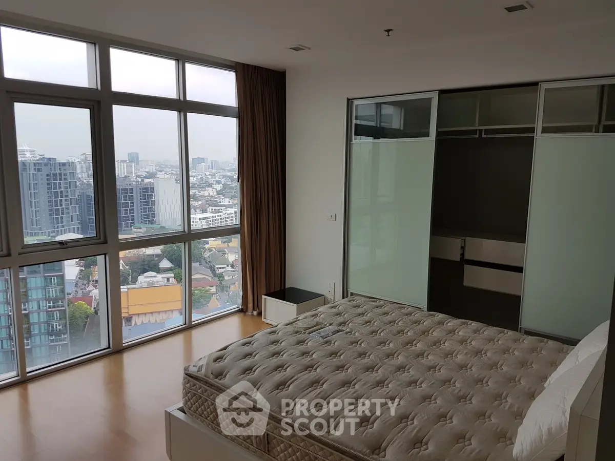 Spacious bedroom with city view and large windows in modern apartment.
