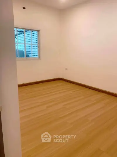 Spacious empty room with wooden flooring and a window, ideal for customization.