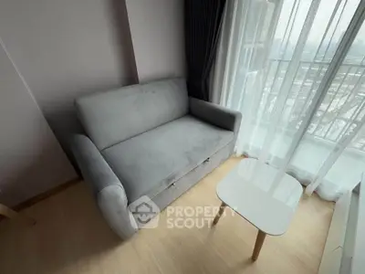 Cozy living room with a plush gray sofa and a small white coffee table by a large window with city view.