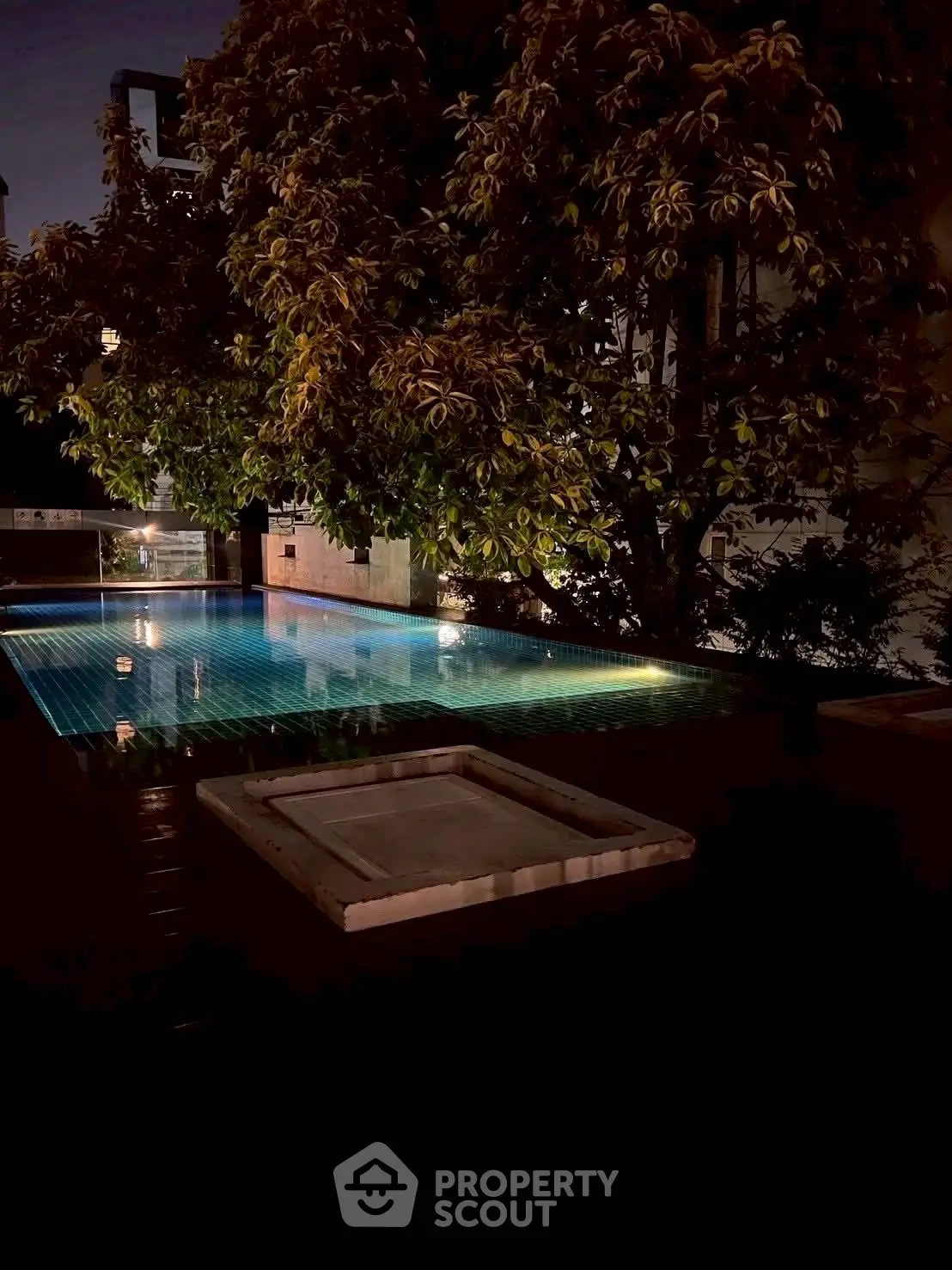 Luxurious night view of a serene outdoor pool surrounded by lush greenery, perfect for relaxation.