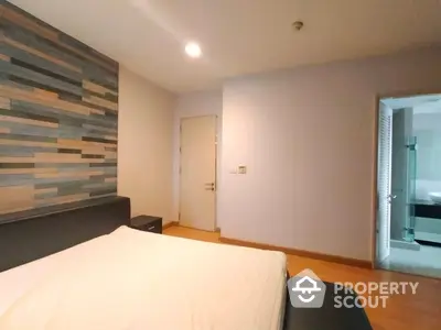 Spacious bedroom with modern wood accent wall and ample natural light, featuring sleek flooring and a peek into the en-suite bathroom.