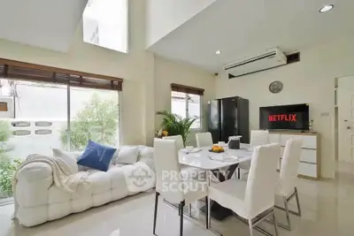 Modern living room with elegant dining area and natural light, featuring a cozy white sofa and stylish decor.