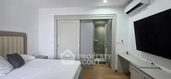 Modern bedroom with ensuite bathroom and wall-mounted TV, featuring sleek design and air conditioning.