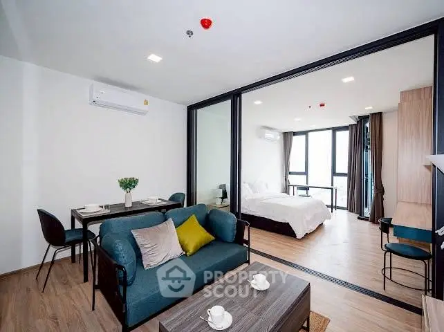 Modern open-plan living room with dining area and bedroom, featuring stylish furniture and large windows.