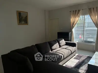 Cozy living room with modern dark sofa and large window, perfect for relaxation.
