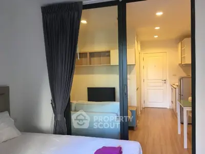 Modern studio apartment with sliding glass doors separating bedroom and living area, featuring sleek kitchen.