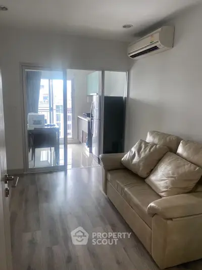 Modern living room with leather sofa and air conditioning, leading to a sleek kitchen with glass doors.