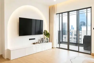 Modern living room with sleek TV setup and balcony view in a high-rise apartment.