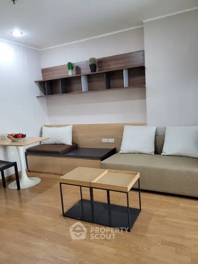 Modern living room with stylish furniture and wooden flooring, featuring a cozy seating area and decorative shelves.