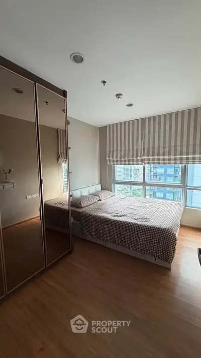 Spacious bedroom with large windows and wooden flooring in modern apartment.