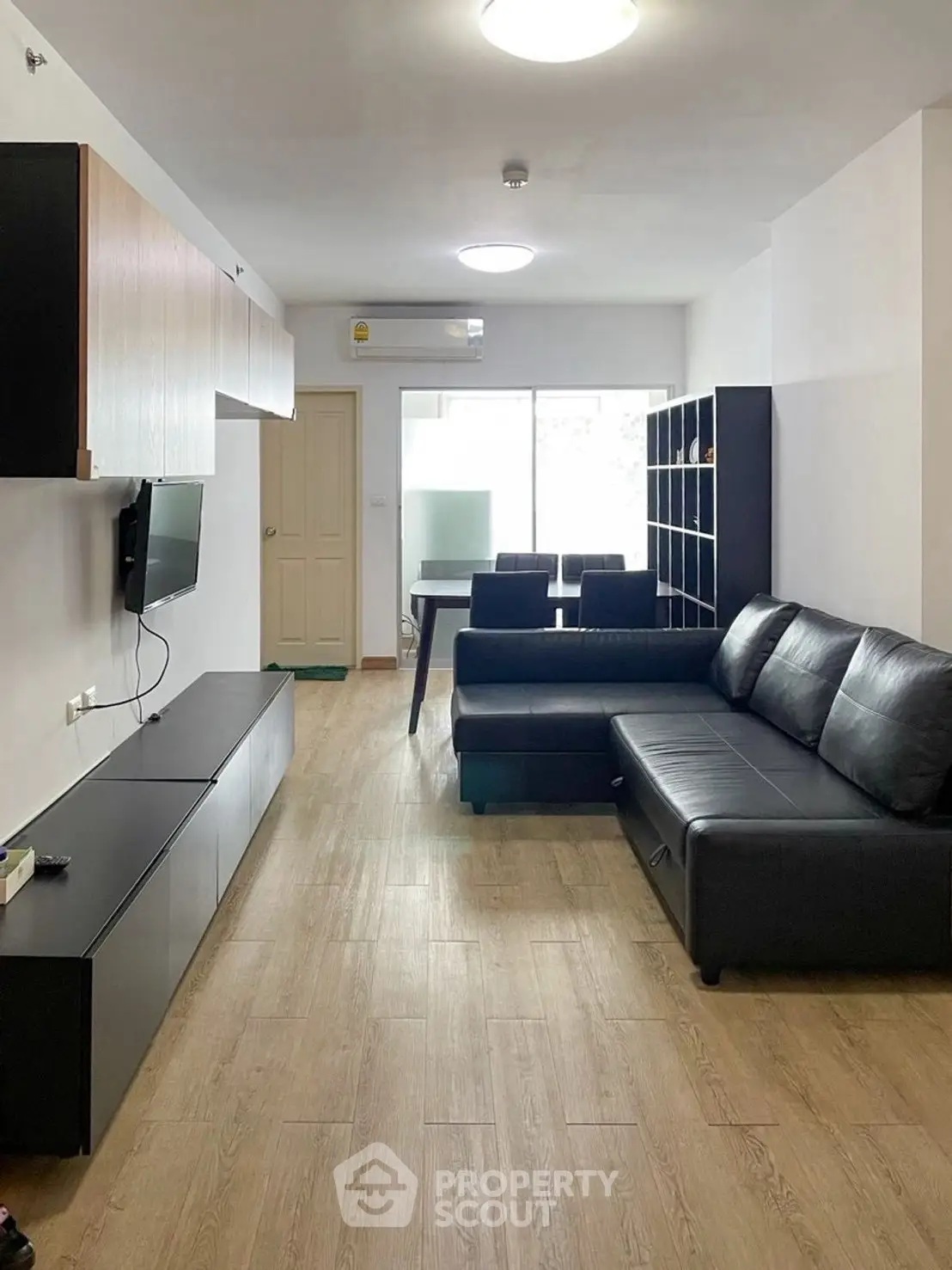 Modern living room with sleek black sofa and wall-mounted TV in open layout apartment.