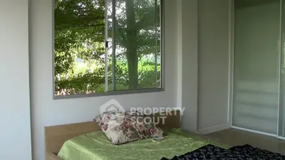 Cozy bedroom with large window offering lush green views, featuring a comfortable bed and floral pillow.