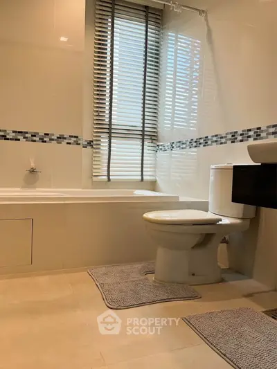 Modern bathroom with bathtub and stylish tiles, featuring natural light through window blinds.