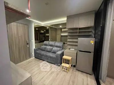 Modern living room with sleek design, featuring a comfortable sofa, mirrored wall, and compact kitchen area.