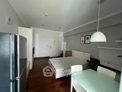 Modern studio apartment with open layout, featuring a cozy bed, dining area, and sleek kitchen appliances.
