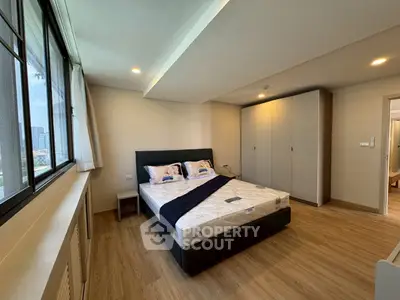 Spacious bedroom with large window and modern furnishings in a high-rise apartment.