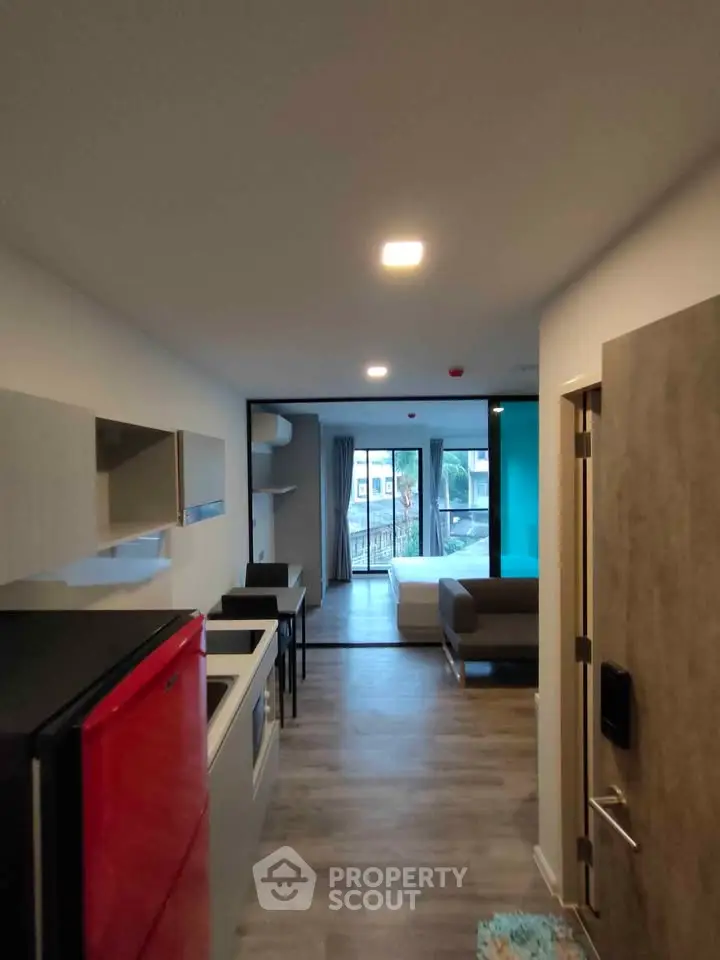 Modern studio apartment with open layout and vibrant red fridge, featuring a cozy living area and bedroom.