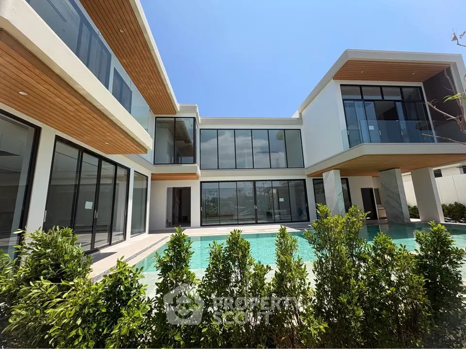 Luxurious modern villa with large windows and private pool, surrounded by lush greenery.
