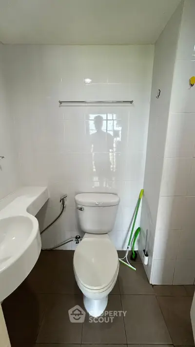 Modern bathroom with sleek white fixtures and tiled flooring, featuring a toilet and sink.