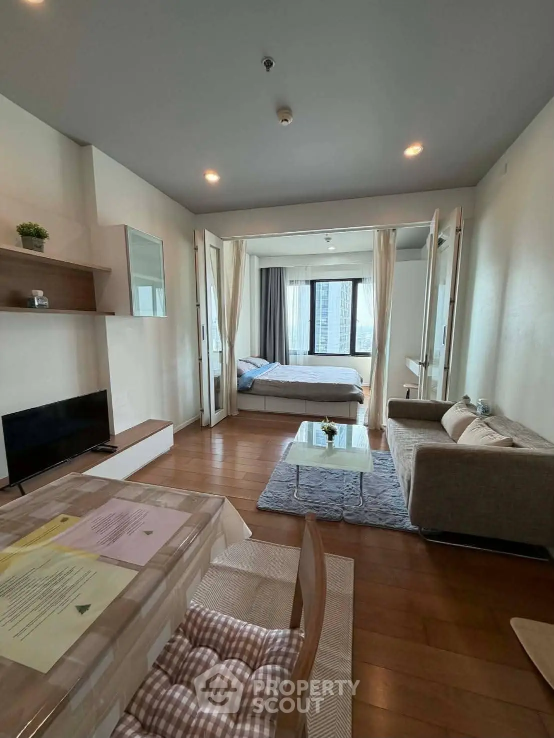 Modern open-plan living room with cozy bedroom and city view, featuring stylish furniture and wooden flooring.
