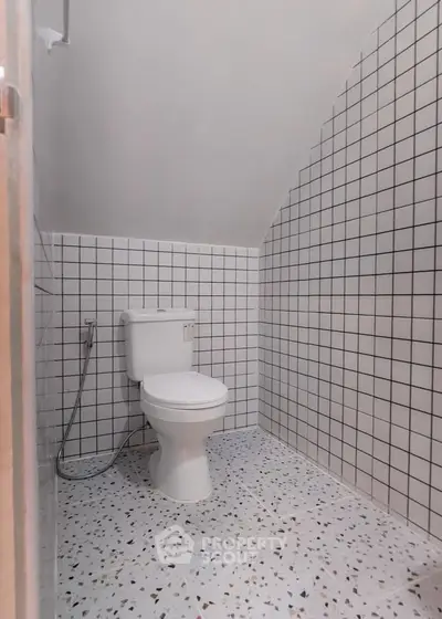 Modern bathroom with white tiled walls and terrazzo flooring, featuring a sleek toilet design.