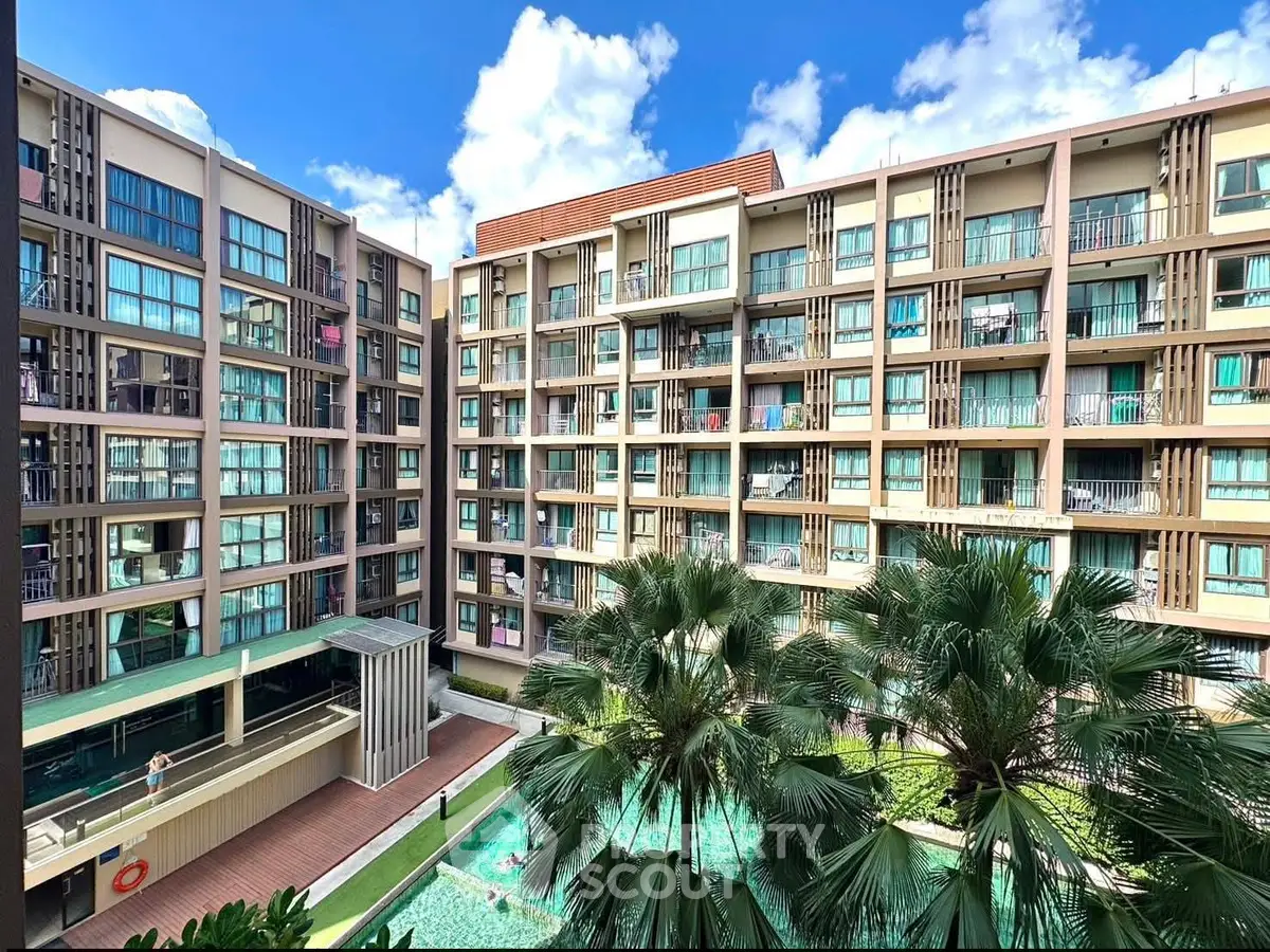 Modern apartment complex with pool and lush greenery under a bright blue sky.