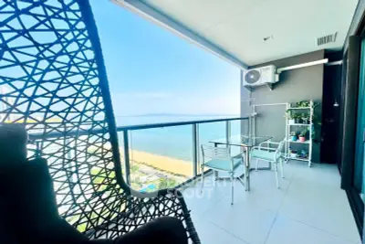 Stunning balcony with ocean view, modern seating, and glass railing in high-rise apartment.