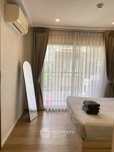 Bright bedroom with large window and balcony access, featuring modern decor and air conditioning.