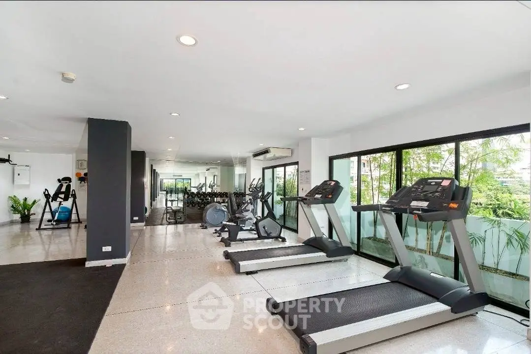 Spacious modern gym with large windows and state-of-the-art equipment in a luxury residential building.