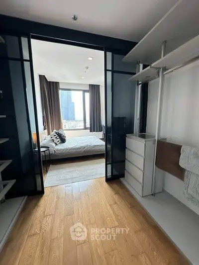 Modern bedroom with wooden flooring and city view, featuring sleek storage solutions and large windows.