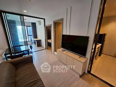 Modern living room with sleek furniture and large TV, open layout leading to bedroom and kitchen.