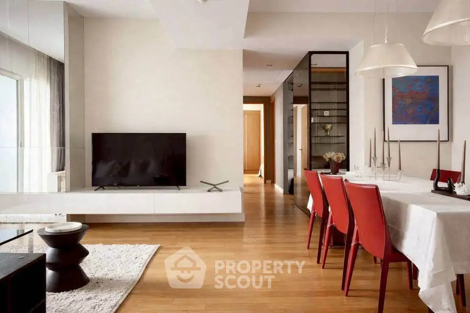 Modern living room with sleek TV setup and elegant dining area featuring red chairs and wooden flooring.